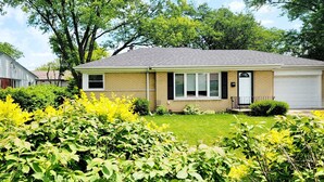 A single-story house with a front garage, surrounded by lush green lawns and yellow flowering bushes. - 4 Bedroom, 2 Full Bath. Centrally Located. Near O'Hare Airport and attractions   (Glenview)