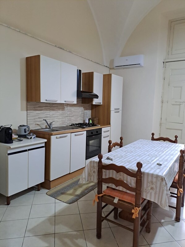 A compact kitchen with white and wooden cabinets, a gas stove, an oven, and a dining table with chairs.