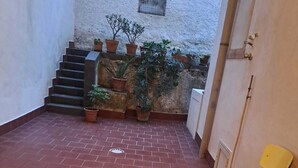 Ein Innenhof mit Terrakottafliesen, einem gelben Stuhl und Kübelpflanzen.