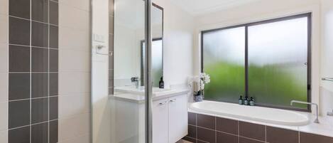A modern bathroom with a glass shower enclosure, a large window with frosted glass, and a white sink with a mirror.
