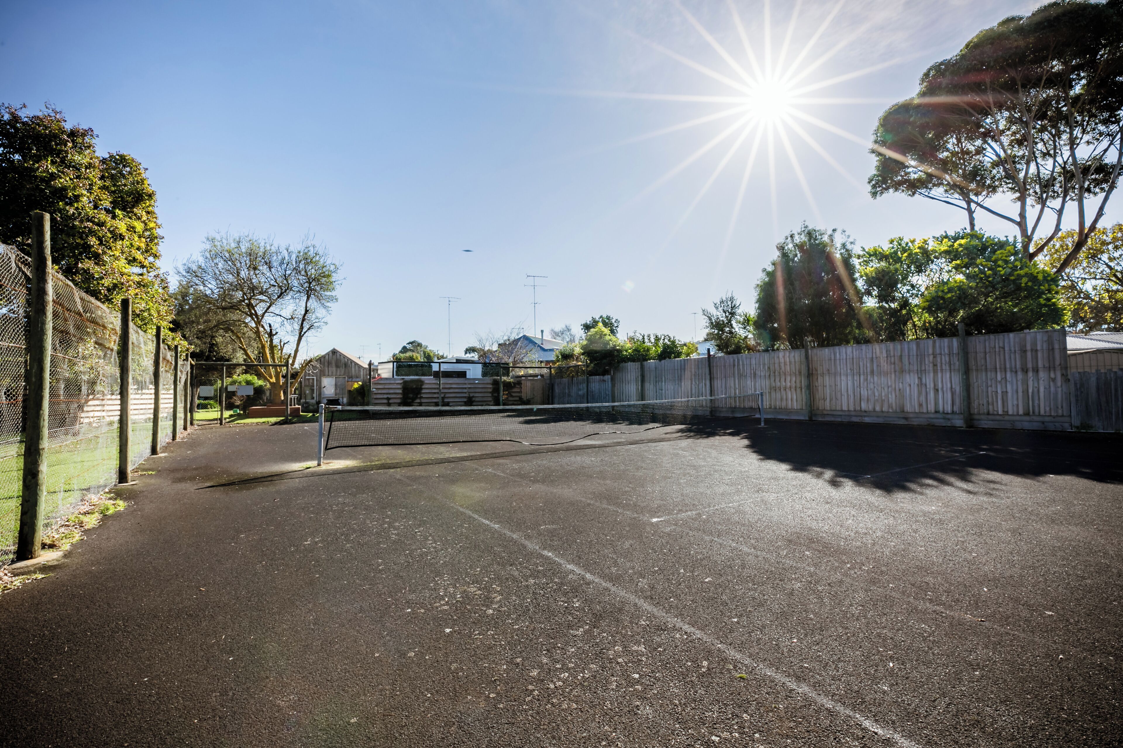 Una cancha de tenis con valla, árboles y cielo despejado.