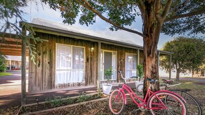 Ein Holzbau mit Veranda, einem rosa Fahrrad und einem Baum.