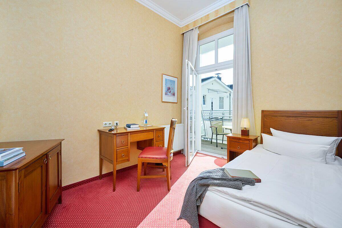 A hotel room with a bed, a desk, a chair, and a window with a view of buildings.
