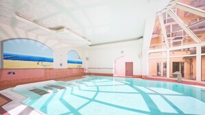 Una piscina interior con paredes de vidrio transparente, vistas a la playa y un diseño arquitectónico moderno.