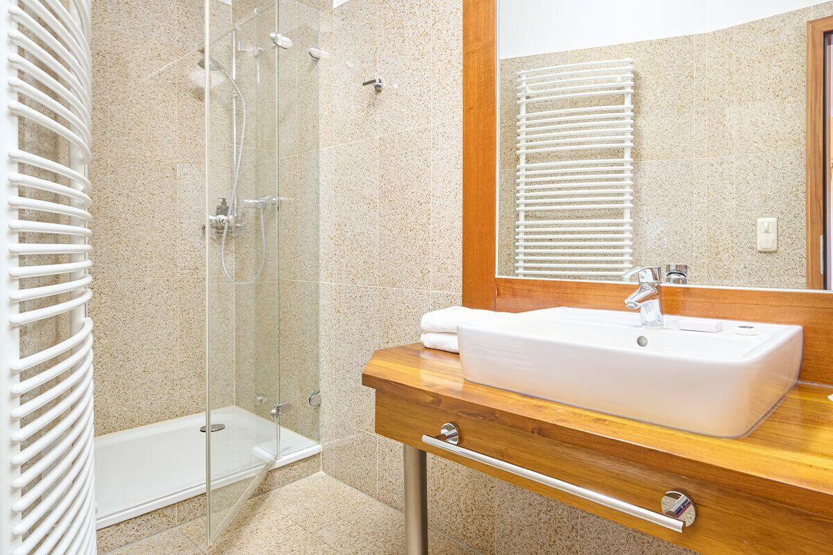 Un baño con cabina de ducha de vidrio, tocador de madera con lavamanos blanco y un espejo grande.