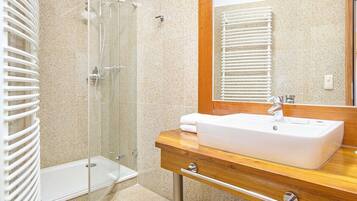 Un baño con cabina de ducha de vidrio, tocador de madera con lavamanos blanco y un espejo grande.