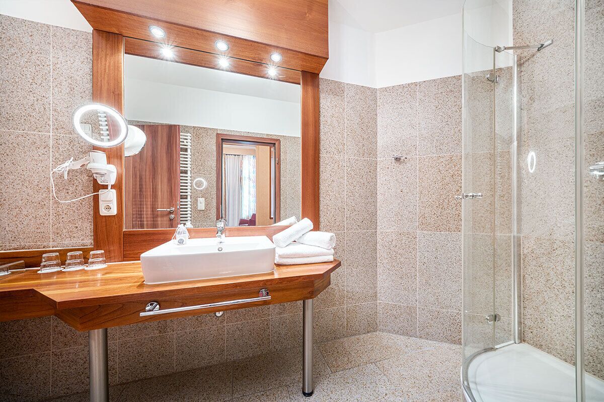A modern bathroom with a wooden vanity, a large mirror, a glass shower enclosure, and a toilet.