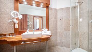 A modern bathroom with a wooden vanity, a large mirror, a glass shower enclosure, and a toilet.