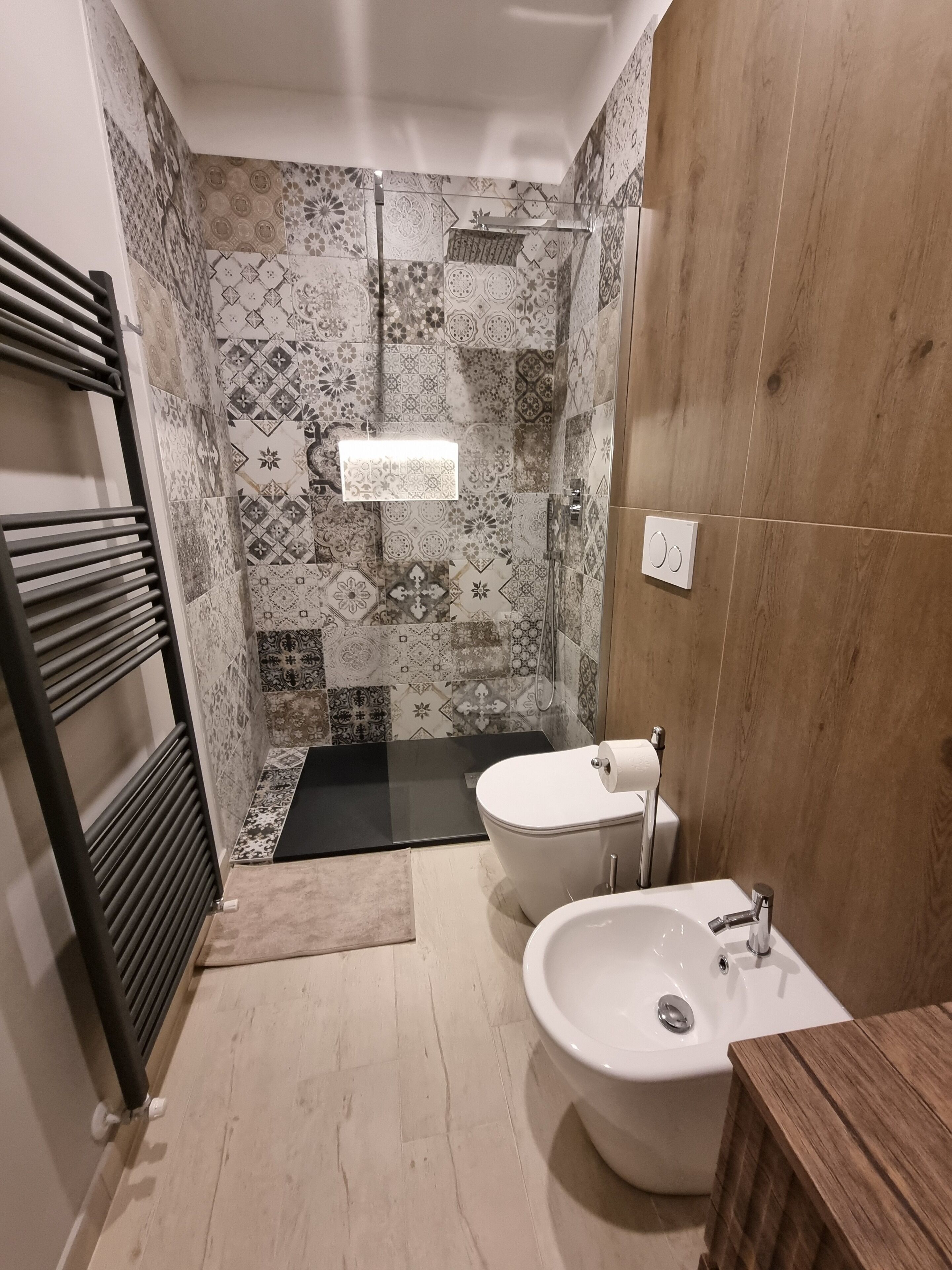 Une salle de bain avec des carreaux décorés, une douche, des toilettes et un bidet.