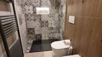 Une salle de bain avec des carreaux décorés, une douche, des toilettes et un bidet.