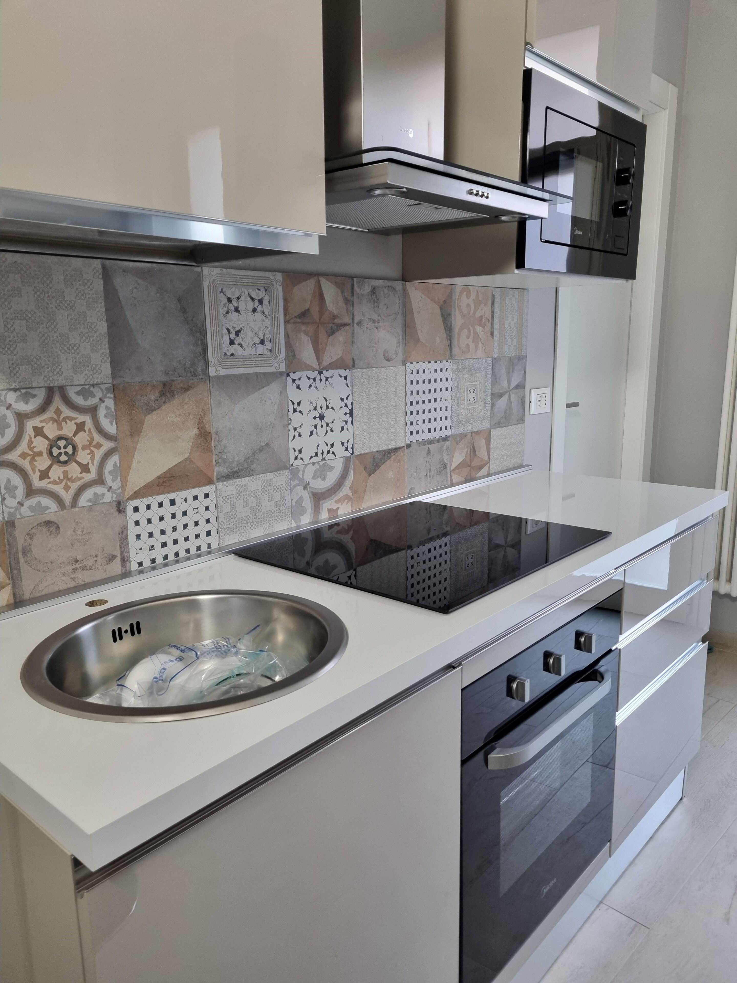Una cocina moderna con un lavamanos de acero inoxidable, una placa de inducción negra y un microondas.