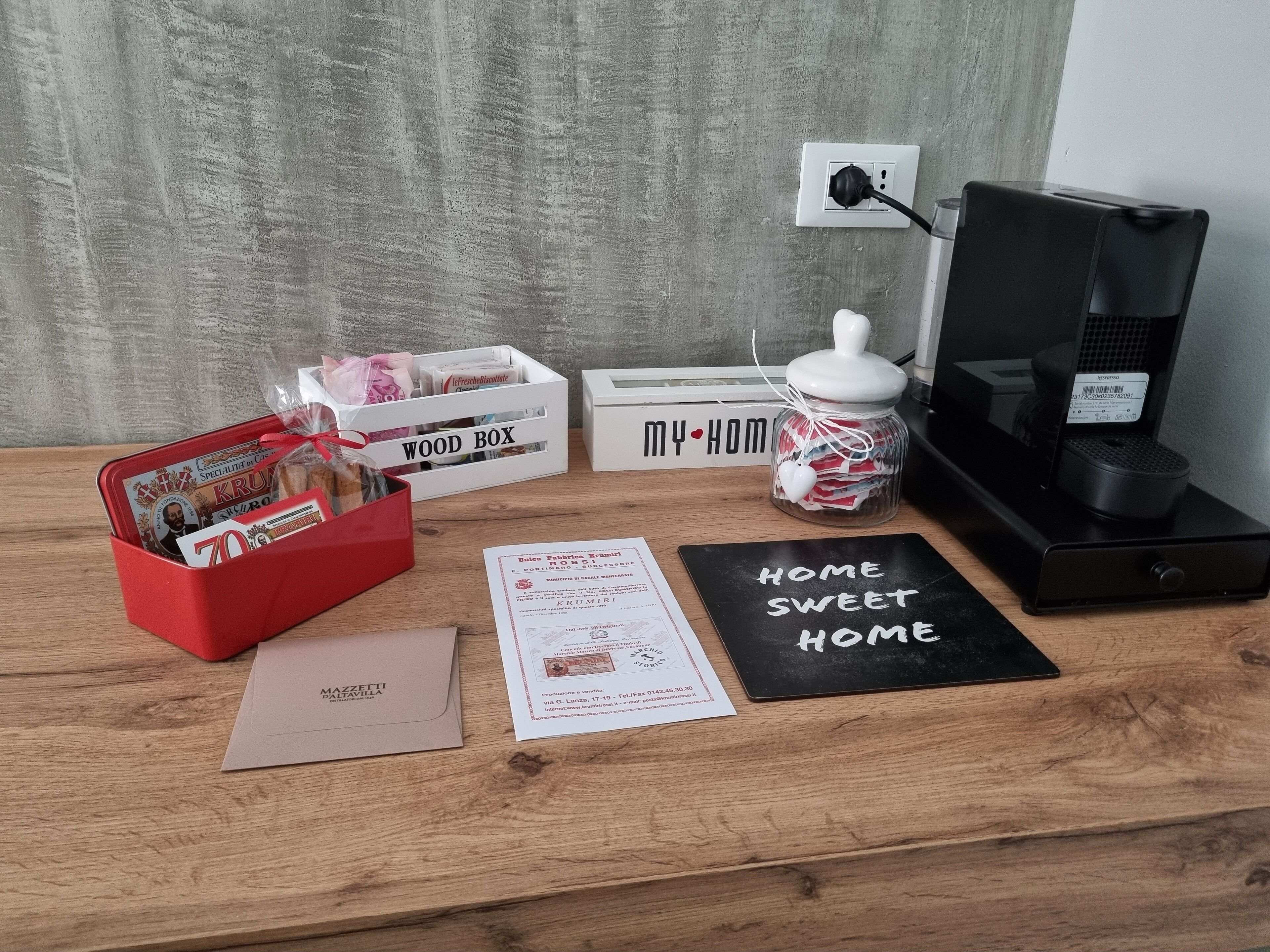 A wooden desk with a red box, a white box labeled "WOOD BOX", a jar with a heart-shaped lid, a black box with "HOME SWEET HOME" written on it, and a white sign with "MY HOM".