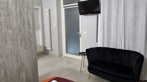 A modern hotel room with a bed, a black armchair, a flat-screen TV mounted on the wall, and a door leading to another room. - CÀ Fiamma 2 Affitti Brevi (Casale Monferrato)