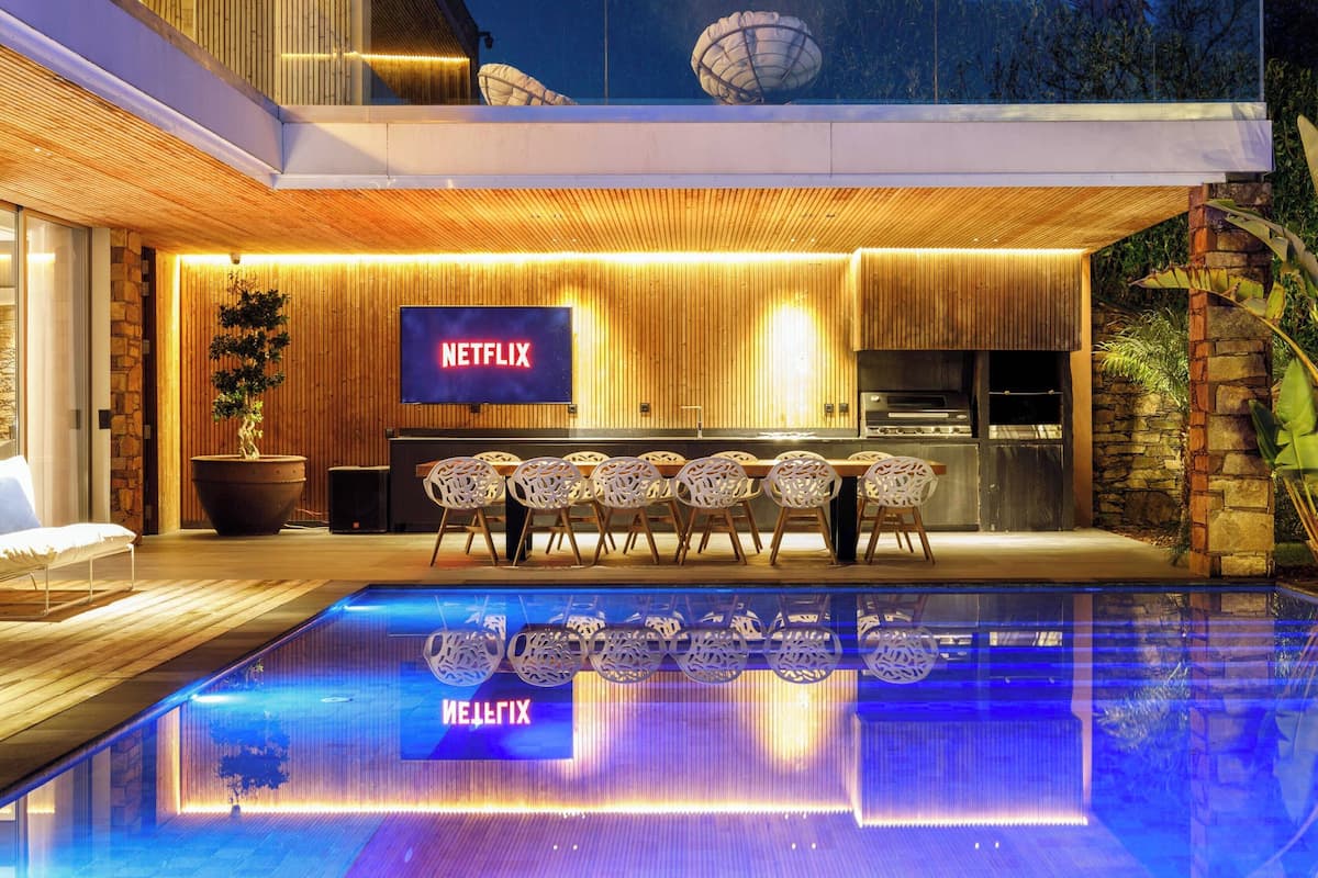 A modern outdoor pool area with a Netflix sign, a stone wall, and a wooden ceiling.