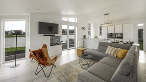 Een moderne woonkamer met een grijze bank, een bruine leren fauteuil en een flatscreen televisie aan de muur.