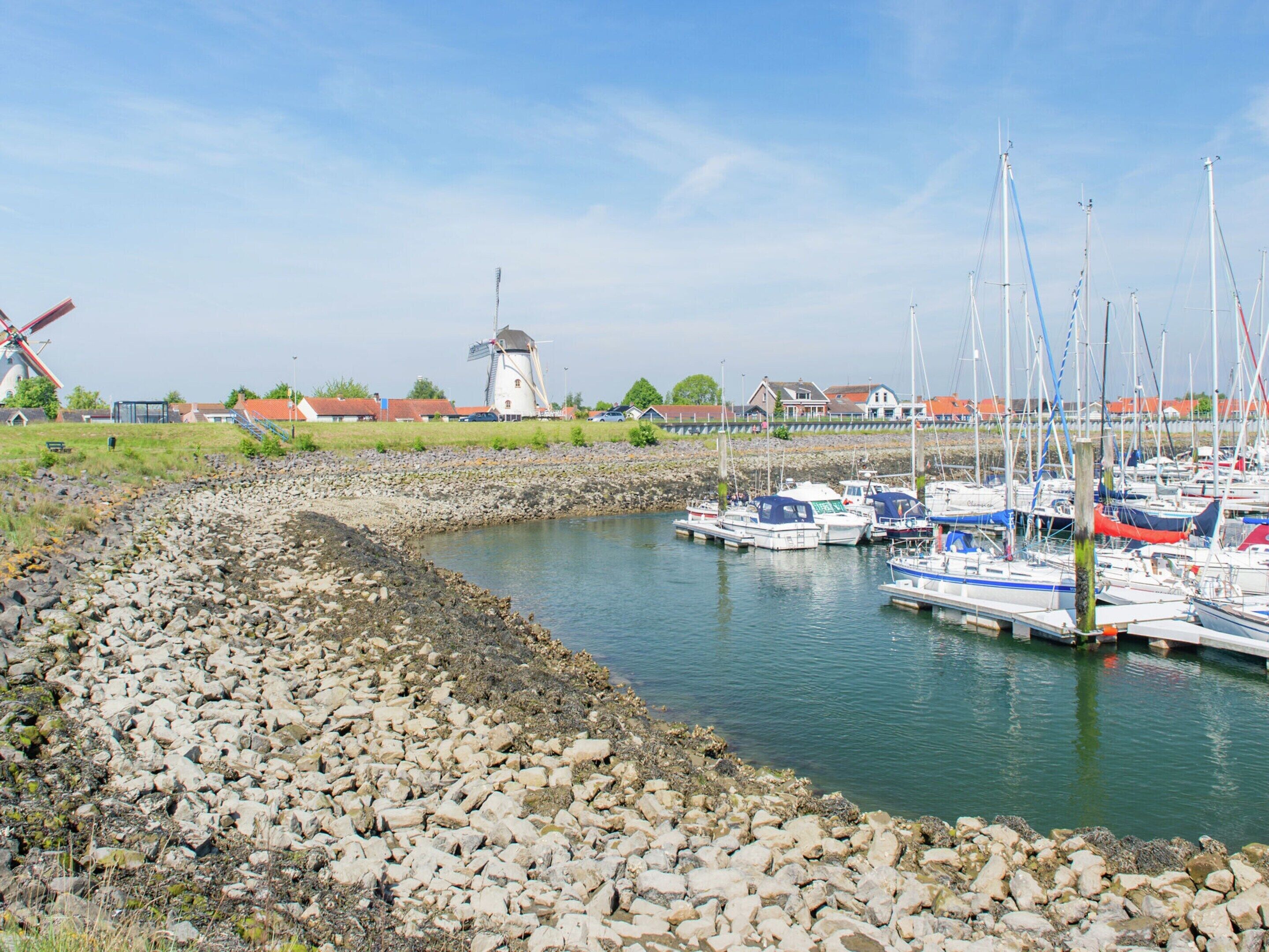 Ein Yachthafen mit vor Anker liegenden Booten, ein Windrad im Hintergrund und eine felsige Küstenlinie.