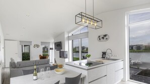 Een moderne keuken met een centraal eiland, een eetgedeelte met stoelen en een groot raam met uitzicht op een waterpartij.