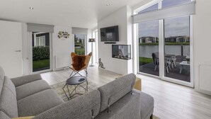 Een moderne woonkamer met grijze banken, een bruine fauteuil en een televisie aan de muur.