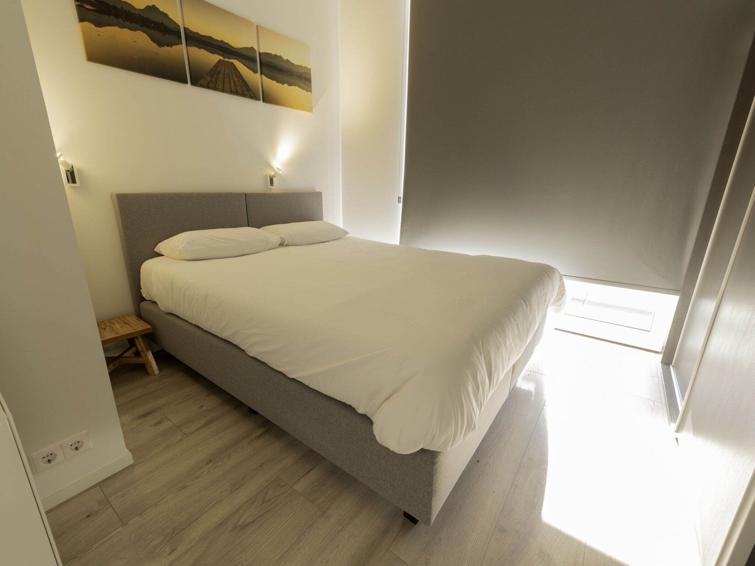 Un dormitorio con una cama, una mesita de noche, una lámpara de pared y un cuadro sobre la cama.