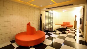 A room with a checkered floor, a curved orange sofa, a white brick wall, and a sliding door leading to another room. - Hip Spa Motel (Taichung)