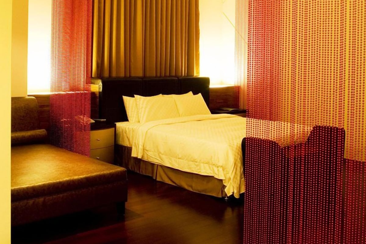 Una habitación de hotel moderna con cama, sofá, escritorio y un amplio ventanal con cortinas.