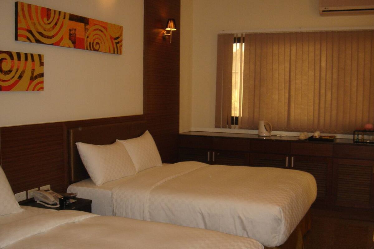 Habitación de hotel con dos camas, una mesita de noche con teléfono, una lámpara y una ventana con cortinas.