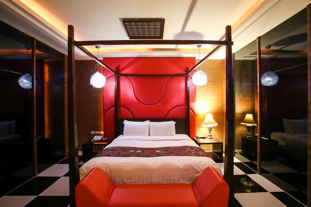 Una cama con dosel y un cabecero rojo, lámparas de noche y un piso a cuadros.