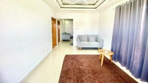 Una sala de estar moderna con un tapete marrón, un sofá gris, una mesita de madera y un ventanal con cortinas oscuras.