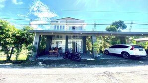 Una casa de dos pisos con un porche cubierto, una motocicleta estacionada y un coche blanco.