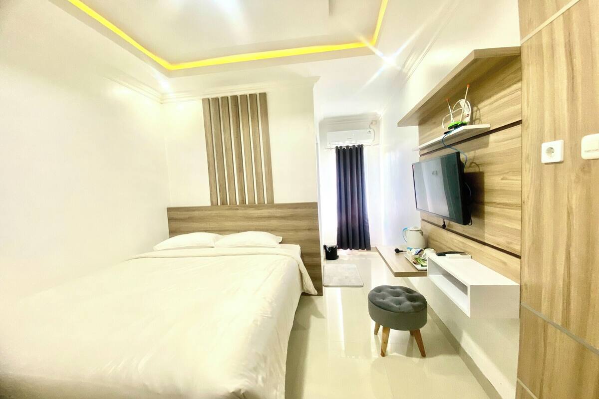 A hotel room with a bed, a desk, a television, and a wall-mounted shelf.