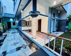 Un bâtiment moderne doté d’une allée dallée, d’une colonne centrale et d’un petit espace extérieur aménagé pour s’asseoir.