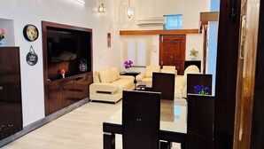 A spacious living room with a sofa set, a dining table with chairs, a TV, and a wooden cabinet.