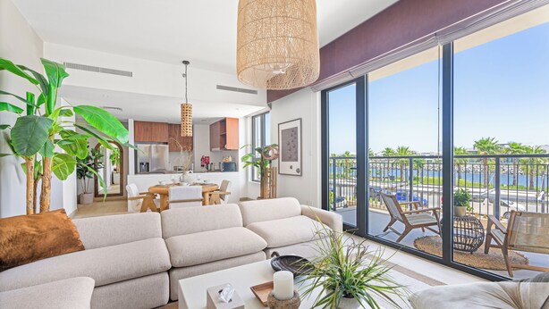 Un salon moderne avec un grand canapé, une table basse et une vue sur un balcon aménagé avec des sièges d’extérieur.