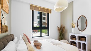 Une chambre moderne avec un grand lit, une table de chevet dotée de paniers, un miroir rond et une fenêtre donnant sur l’extérieur.