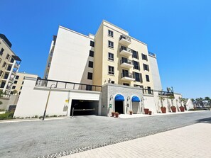Un immeuble à plusieurs étages doté d’une façade sobre, d’une entrée centrale surmontée d’un auvent bleu et de balcons avec des garde-corps noirs.
