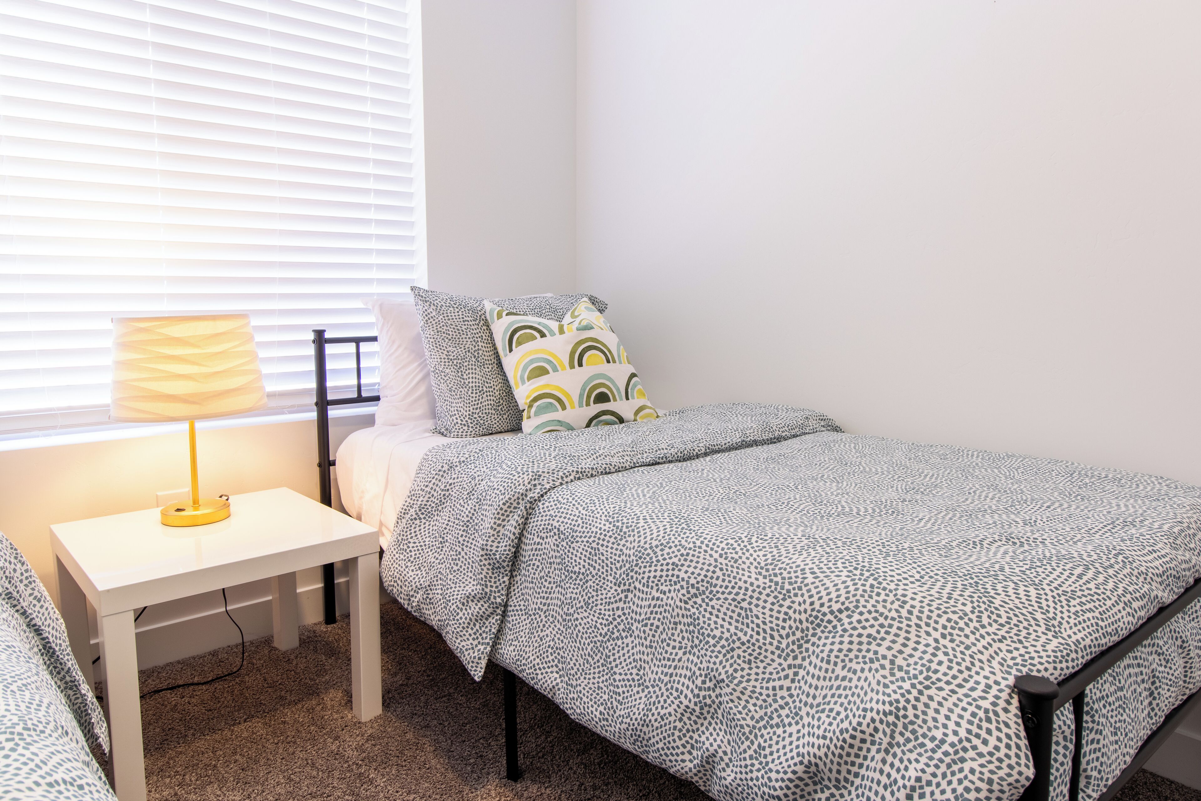 Quarto com uma cama de solteiro, mesa de cabeceira com abajur e janela com persianas.