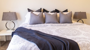 A neatly made bed with a patterned bedspread and multiple pillows, flanked by two bedside tables with lamps.