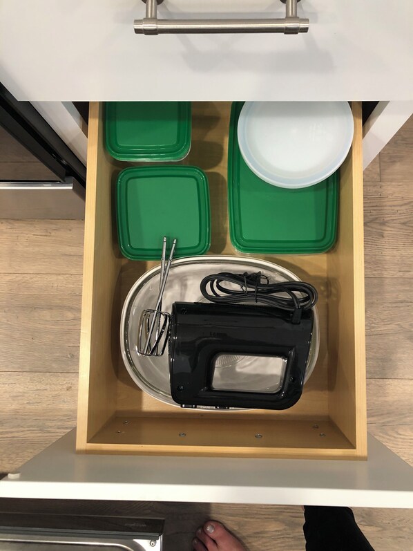 Un cajón de cocina con contenedores de almacenamiento verde, un plato blanco y un electrodoméstico negro.