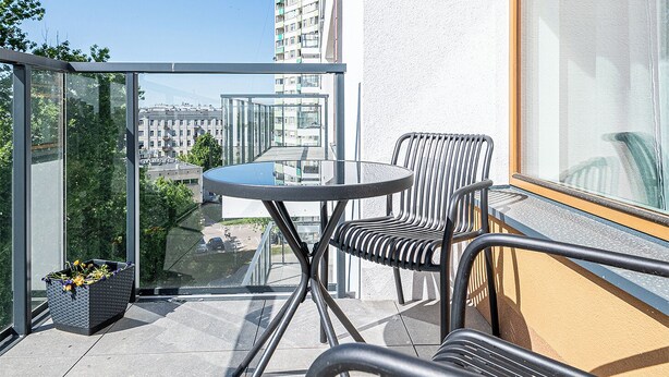 A balcony with a table and chairs, a potted plant, and a view of buildings. - Apartament Ludwiki (Warsaw)