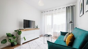 A modern living room with a green sofa, a flat-screen TV on a wooden console, a potted plant, and a white rug. - Apartament Ludwiki (Warsaw)