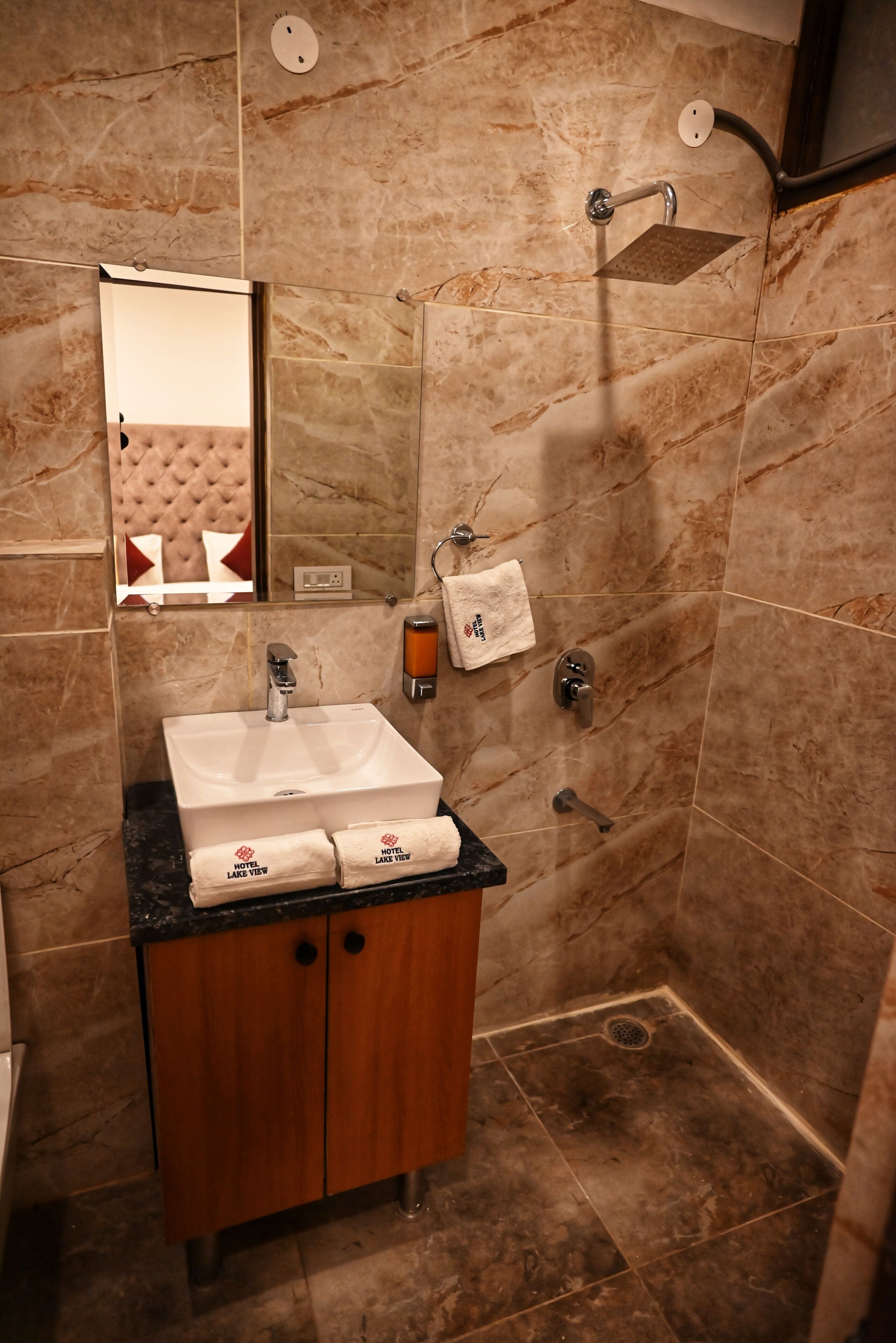 A bathroom with a marble-tiled shower, a sink with a towel, and a wooden cabinet.