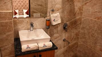 A bathroom with a marble-tiled shower, a sink with a towel, and a wooden cabinet.