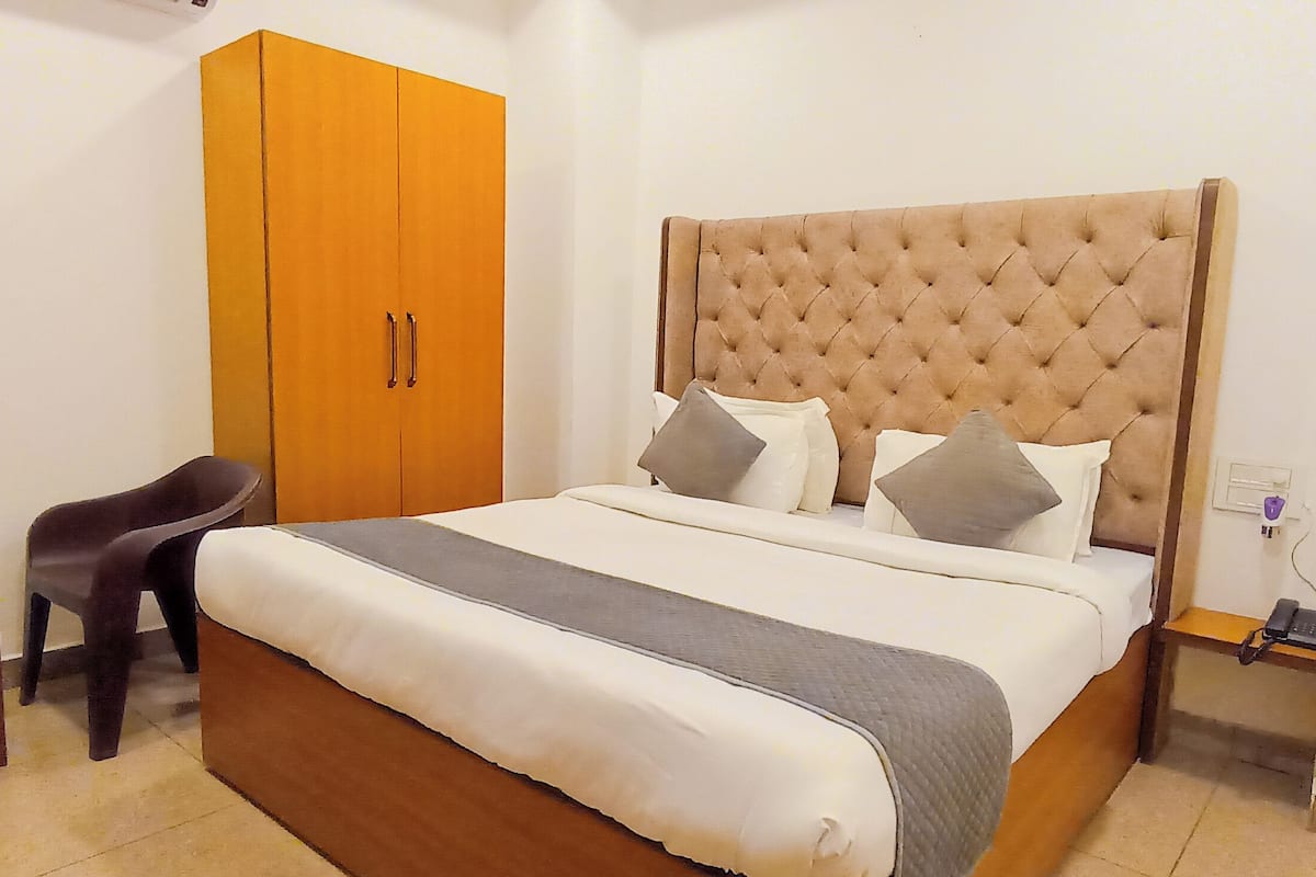 A bedroom with a large bed, a wooden wardrobe, a small table with a kettle, and a chair.