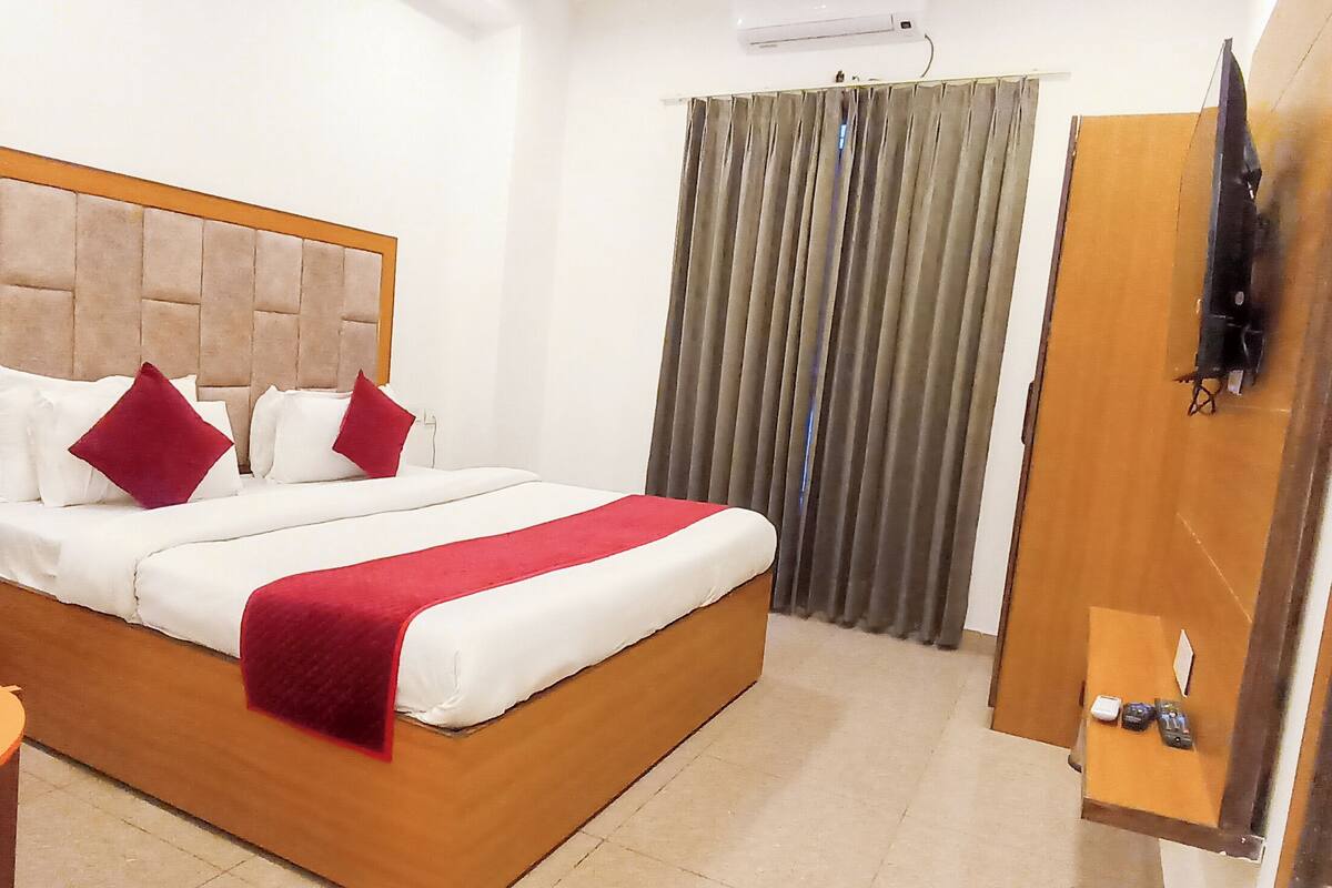 A hotel room with a bed, a nightstand, a table, a TV, and a curtain.