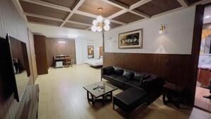 Ein Wohnzimmer mit einer Couch, einem Couchtisch und einem Fernseher. Die Decke besteht aus Holz und an der Wand hängt ein Gemälde.