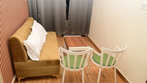 A small room with a brown sofa, two white chairs with green cushions, and a wooden coffee table. - Green Park (Varanasi)