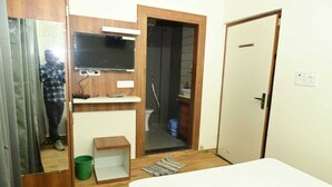A compact room with a bed, a small wooden cabinet, a television, and a bathroom visible through an open door. - Green Park (Varanasi)