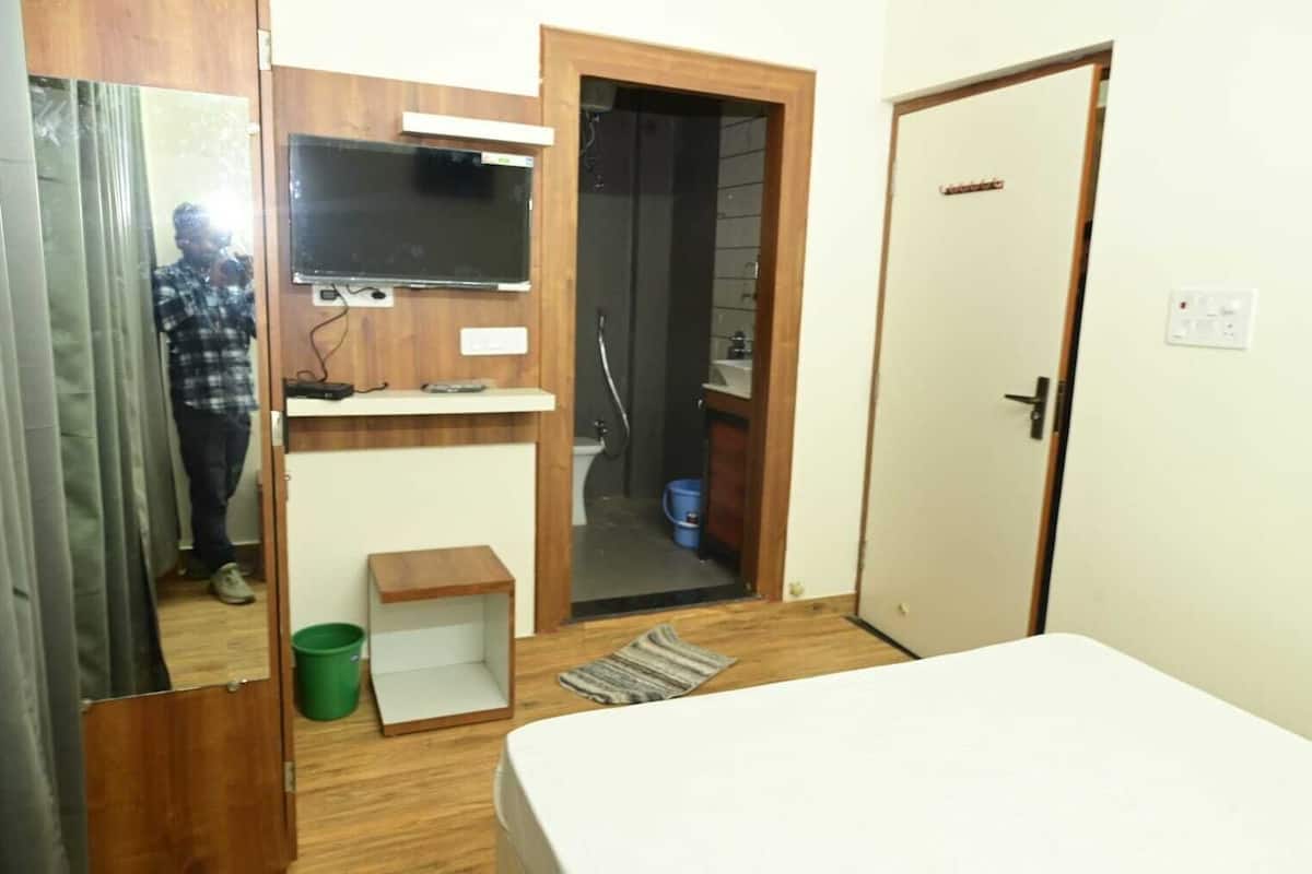A compact room with a bed, a small wooden cabinet, a television, and a bathroom visible through an open door.