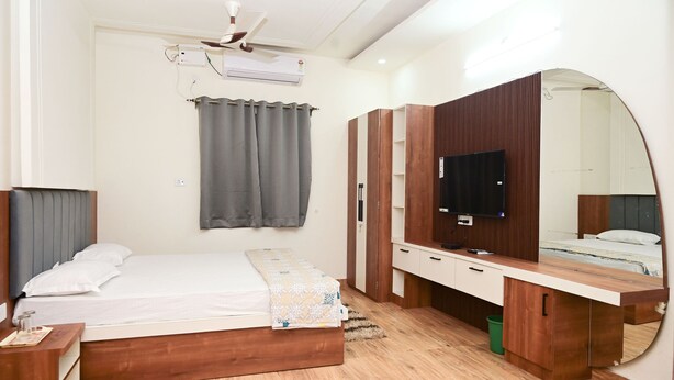 A modern bedroom with a bed, a vanity with a mirror, a ceiling fan, and a TV. - Green Park (Varanasi)