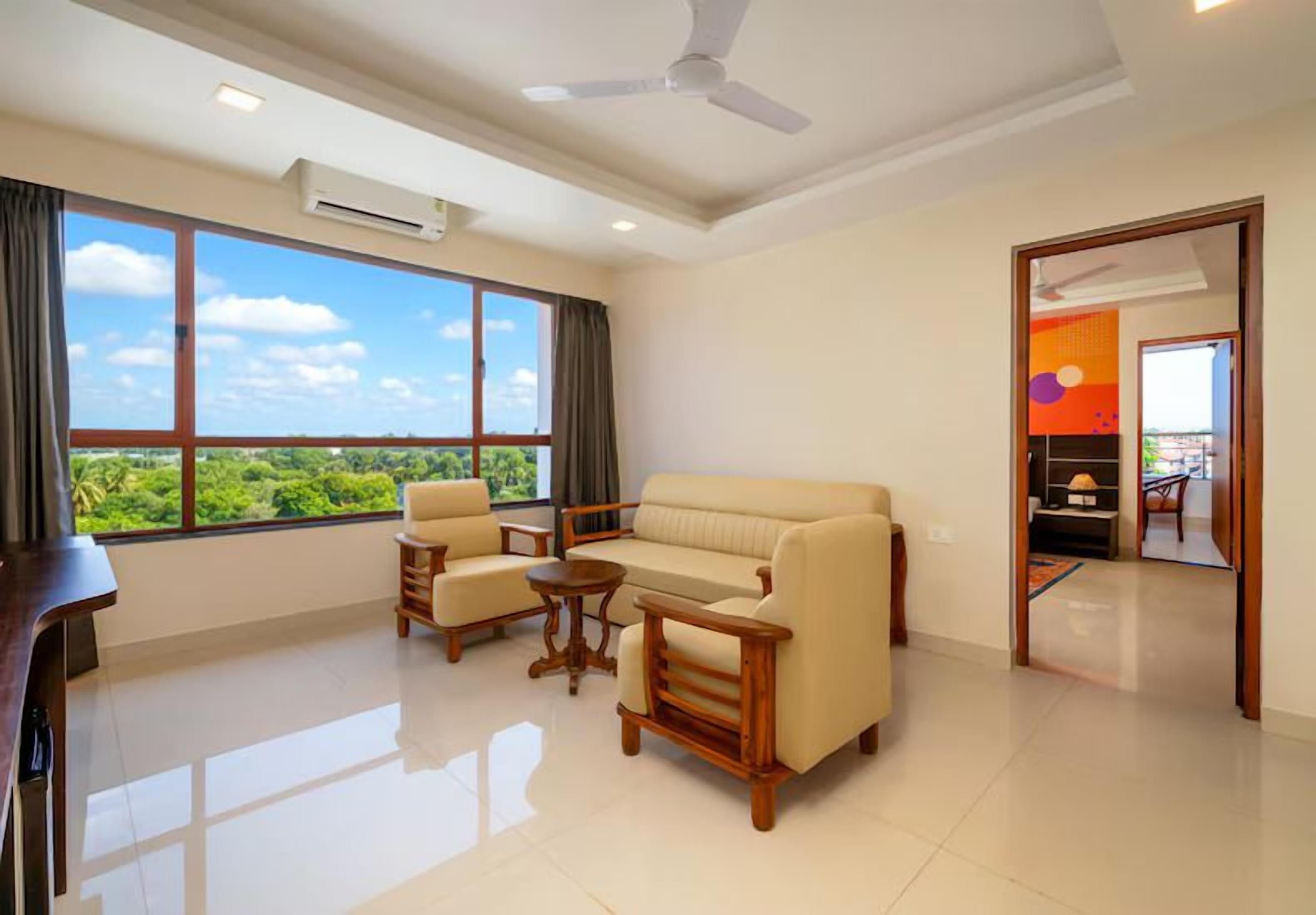 A spacious living room with a sofa, two armchairs, a coffee table, and a ceiling fan.